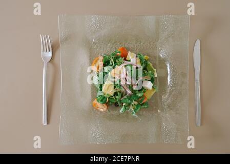 De dessus de savoureuse salade avec des cubes de mozzarella frais, des tomates et de fines tranches d'oignon rouge décorées avec de la sauce moutarde dans une assiette transparente en verre à proximité des couverts Banque D'Images