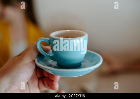 Crop personne non reconnaissable tenant soucoupe en céramique bleue et tasse de thé aromatique chaud sur fond flou dans le café Banque D'Images