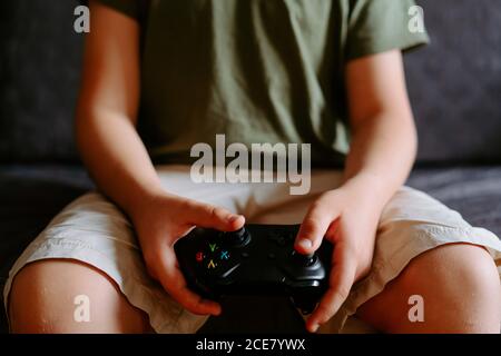 Adorable petit garçon en train de vivre la réalité virtuelle dans des lunettes modernes jouer sur un canapé avec une manette de jeu à la maison Banque D'Images