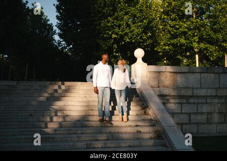 Ensemble complet positif et varié en ensembles décontractés escalier dans la rue tout en tenant les mains doucement et en regardant Les uns les autres avec amour le soir à Madrid Espagne Banque D'Images