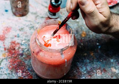 De dessus rogner un artiste anonyme homme lavant le pinceau dans bol avec eau colorée au-dessus du plan de travail en studio Banque D'Images