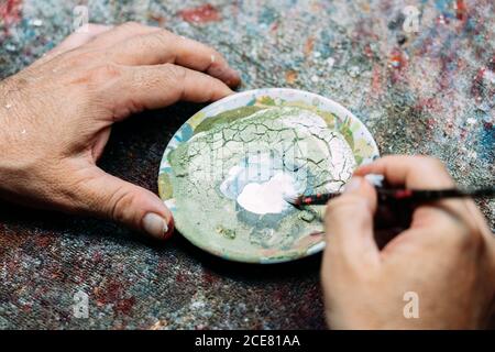 Récolte concentrée mature homme artiste portant des lunettes mélangeant bleu et des peintures blanches dans la palette tout en travaillant dans un atelier créatif Banque D'Images