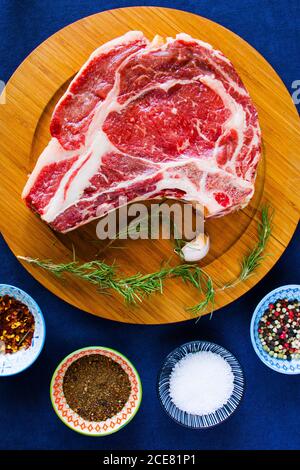 Viande de bœuf crue sur la table, épices et ingrédients pour le romarin et le steak de côtes. Poivre et gros sel Banque D'Images