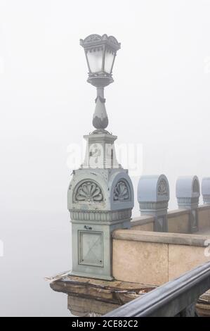 Ancien lampadaire ornemental placé sur la clôture en pierre de l'ancien pont le jour brumeux de la ville Banque D'Images