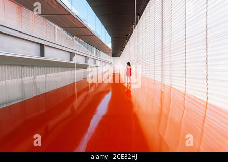 Vue arrière d'une femme méconnue sur un sol orange brillant de passage dans un bâtiment moderne Banque D'Images