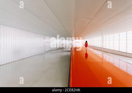 Vue arrière d'une femme méconnue sur un sol orange brillant de passage dans un bâtiment moderne Banque D'Images