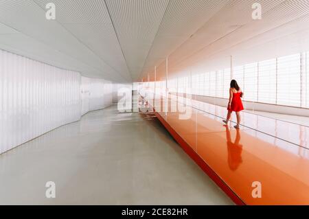 Vue arrière d'une femme méconnue sur un sol orange brillant de passage dans un bâtiment moderne Banque D'Images