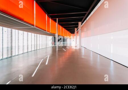 Vue latérale d'une femelle non reconnaissable, debout sur du béton gris brillant étage de passage dans un bâtiment moderne orange Banque D'Images