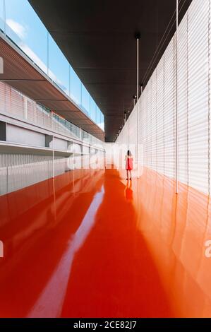 Vue arrière d'une femme méconnue sur un sol orange brillant de passage dans un bâtiment moderne Banque D'Images