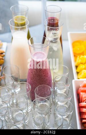 Grand angle de smoothie assortis dans des bouteilles en verre placées dessus table avec verres vides pour la fête Banque D'Images