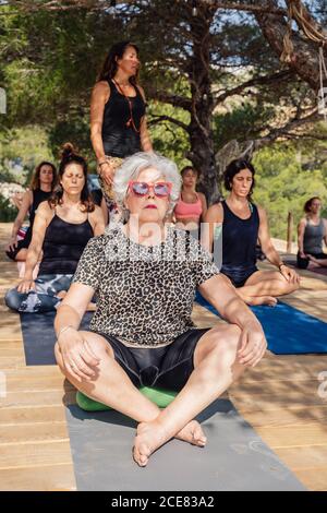 Pleine longueur focalisée mature femelle dans lotus poser méditant pendant pratiquer le yoga en plein air assis sur un podium en bois Banque D'Images