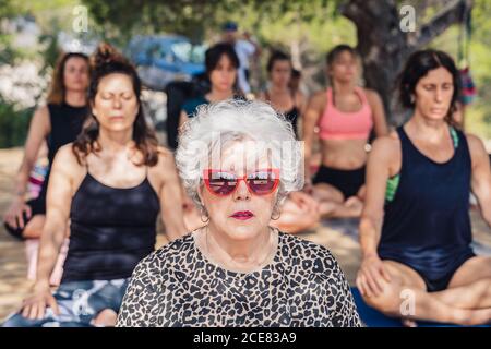 La femme mûre concentrée dans le lotus pose méditant tout en pratiquant le yoga en plein air assis sur un podium en bois Banque D'Images