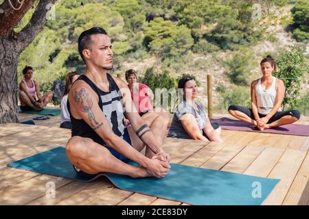 Plongeurs concentrés étudiants de yoga dans des vêtements actifs faisant ouverture de hanche Baddha Konasana position pendant les cours en plein air en été Banque D'Images