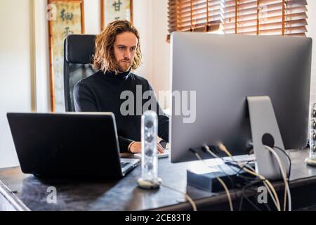 Homme indépendant sérieux assis dans le bureau à domicile et dactylographiant sur clavier pendant le travail sur le projet Banque D'Images