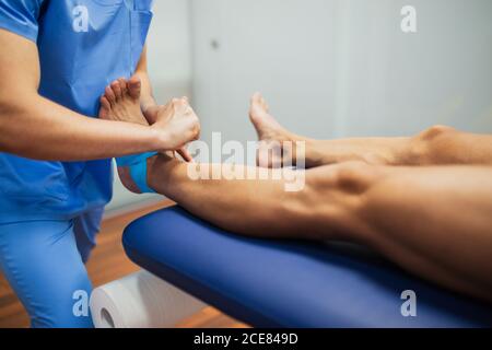 Vue de dessus de la récolte chiropracteur non reconnaissable en bleu uniforme attachant ruban kinesio sur le pied d'un homme sans visage allongé sur l'examen canapé en clinique Banque D'Images