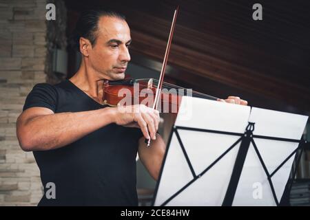 Violoniste hispanique de talent jouant du violon et regardant la musique feuilles pendant la répétition Banque D'Images