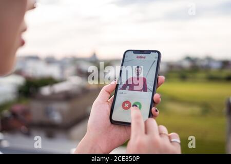 Anonyme femme sélectionnant l'homme tout en se reposant sur la terrasse et en parcourant l'application de rencontres sur smartphone Banque D'Images