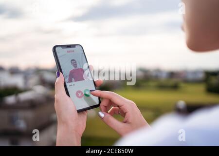 Anonyme femme sélectionnant l'homme tout en se reposant sur la terrasse et en parcourant l'application de rencontres sur smartphone Banque D'Images