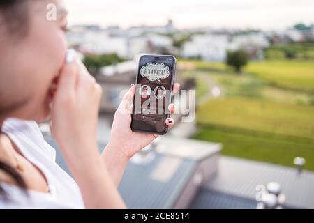 Anonyme femme sélectionnant l'homme tout en se reposant sur la terrasse et en parcourant l'application de rencontres sur smartphone Banque D'Images