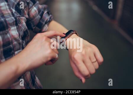 Vue latérale d'une petite femme anonyme en chemise à carreaux décontractée vérification de l'heure sur le bracelet intelligent Banque D'Images