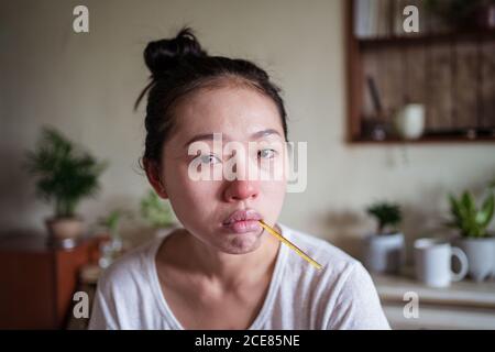 Femme ethnique épuisée assise sur le lit à la maison et mesurant température avec thermomètre tout en ayant froid et en regardant la caméra Banque D'Images