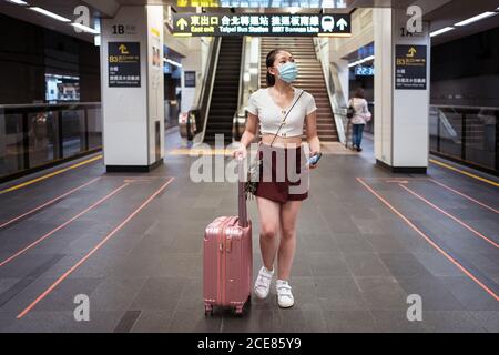 Pleine longueur jeune asiatique femme en mini jupe marche avec valise à la gare en attendant le train Banque D'Images