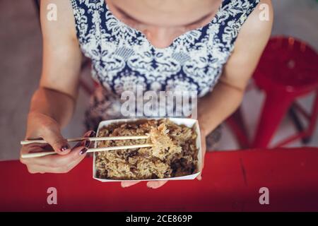 Par-dessus une femelle ethnique non reconnaissable et écourtée assise au comptoir Dans le marché nocturne de Zhubei et manger du riz à l'huile gluante avec baguettes Banque D'Images