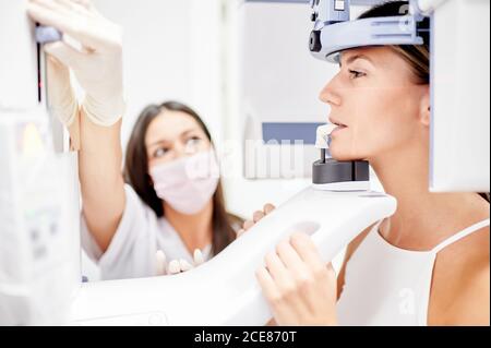 Dentiste féminin utilisant un ordinateur tout en faisant une radiographie à la jeune femme dans la clinique dentaire contemporaine Banque D'Images