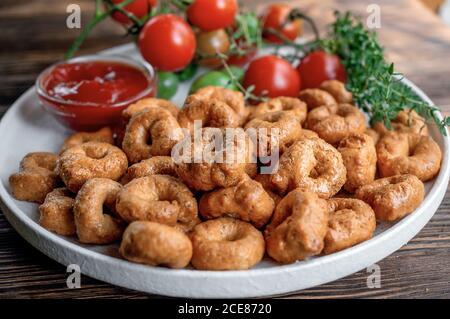 Tortellini fait à la main avec des tomates et des verts de thym sur une plaque blanche est appelé taralli. Taralli dans les boulangeries italiennes dans le sud de l'Italie sur un bois Banque D'Images