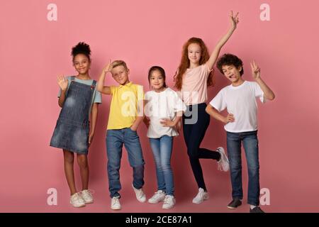 Joyeux écoliers qui fait des visages et montre une variété de gestes sur fond rose, portrait en longueur Banque D'Images