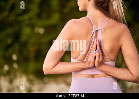 Femme de culture non reconnaissable dans les vêtements de sport pratiquant le yoga avec le geste de Namaste derrière le dos et regardant loin Banque D'Images