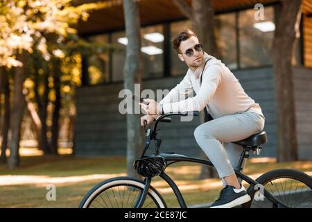 Homme d'affaires à vélo. Guy en lunettes de soleil et smartphone dans le parc Banque D'Images