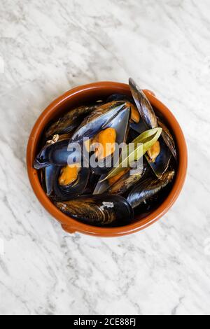 Vue de dessus d'un bol rond rempli de moules fraîchement cuites avec des verts placés sur une table en marbre Banque D'Images