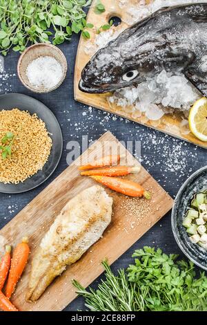 Vue de dessus de poisson frais entier sur des glaçons et le filet frit avec des carottes sur une table noire avec des épices et verts Banque D'Images