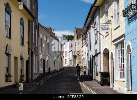 Un homme marche un chien à côté des boutiques traditionnelles et des vieilles maisons colorées sur Axbridge High Street dans Somerset. Banque D'Images