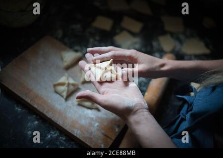 De dessus de la récolte anonyme femme préparant des boulettes carrées similaires avec décoration sur le dessus de la planche à découper avec de la farine près de la broche en bois Banque D'Images