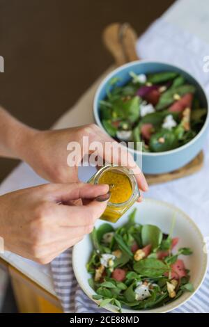 De dessus de la récolte anonyme personne tenant le verre bocal avec sauce pour salade végétarienne à base de feuilles d'étrel et fraîche tranches de pastèque et de pitaya Banque D'Images