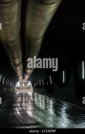 Large passage dans le tunnel minier avec lampes luminescentes sur la pierre murs et énorme tuyau métallique Banque D'Images
