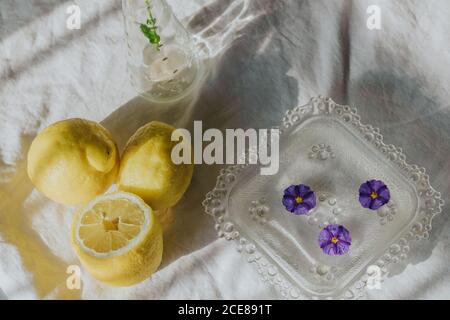 Fleur violette délicate dans vase en verre placé sur la table avec tissu blanc près d'une boisson rafraîchissante et composé de citrons naturels Banque D'Images