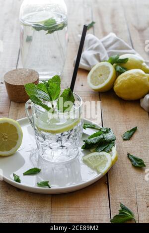Boisson rafraîchissante froide avec soda et citron garni feuilles de menthe fraîche servies sur une tasse en verre avec de la paille table en bois Banque D'Images