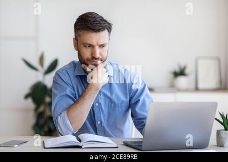 Homme d'affaires attentionné travaillant avec un ordinateur au bureau, regardant l'écran d'un ordinateur portable Banque D'Images