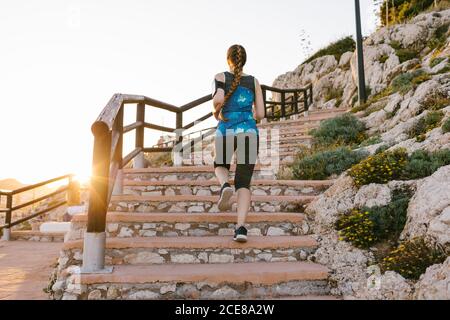 Vue arrière basse d'une Sportswoman non reconnaissable dans un t-shirt et de leggings en train de courir des marches de pierre pendant l'entraînement au coucher du soleil Banque D'Images