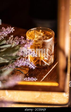 Verre à l'ancienne avec boisson alcoolisée placé sur la table avec fleurs de lavande et reflétées dans le miroir Banque D'Images