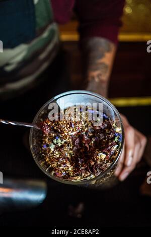 De dessus homme anonyme prenant des herbes séchées de la tasse pendant préparation de la boisson au bar Banque D'Images