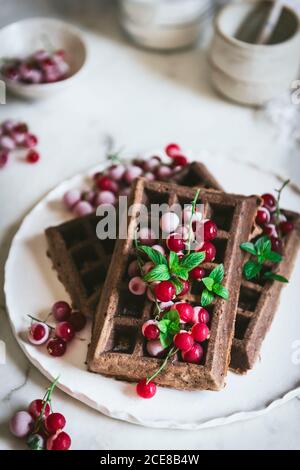 Des gaufres savoureuses au chocolat aux flocons d'avoine avec baies de gooseberries sont servies sur plaque blanche avec cuillère et couteau sur bois clair tableau Banque D'Images