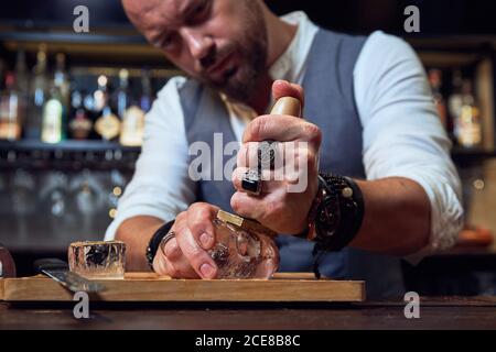 Cube de glace à gratter barman professionnel avec outil en bois sur bois montez à bord tout en préparant un cocktail au bar Banque D'Images