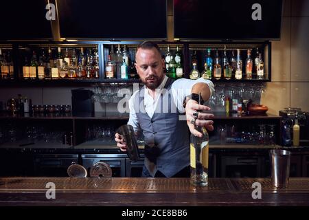 Un jeune barman professionnel tient une bouteille tout en préparant un cocktail la barre Banque D'Images