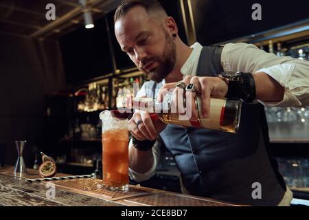 Un jeune barman professionnel tient une bouteille tout en préparant un cocktail la barre Banque D'Images