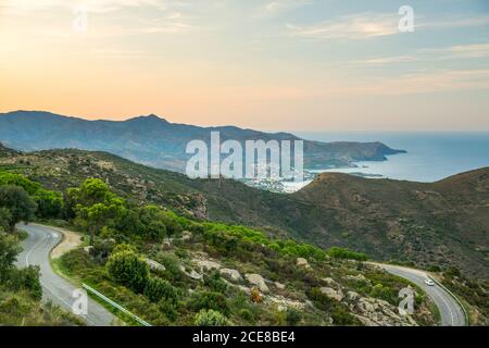 Depuis le dessus du paysage merveilleux de la côte de mer avec la sinueuse Route menant à travers les montagnes rocheuses et les collines verdoyantes près de Cadaques Ville en Espagne en soirée d'été avec ciel nuageux et coloré en arrière-plan Banque D'Images