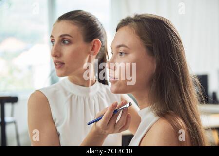 Maquilleuse concentrée faisant des sourcils sur jeune belle cliente féminine paupières en travaillant dans un studio contemporain Banque D'Images